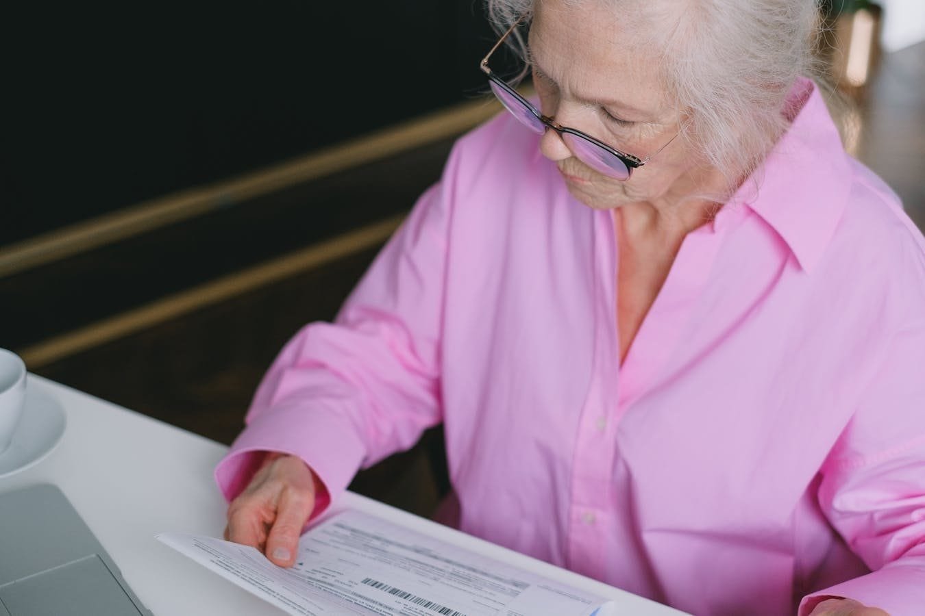 Pensão por Morte: Duração da Cota e Vitaliciedade 1 Elderly woman in pink shirt carefully reading a document indoors.
