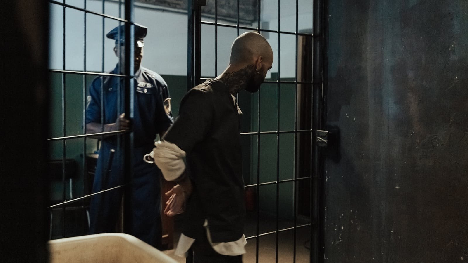 Police officer escorting a handcuffed prisoner through a dimly lit jail corridor.