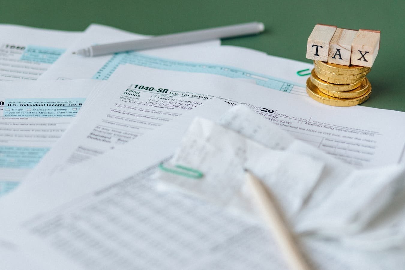 Stack of tax forms and coins with a TAX stamp, symbolizing finance and accounting.