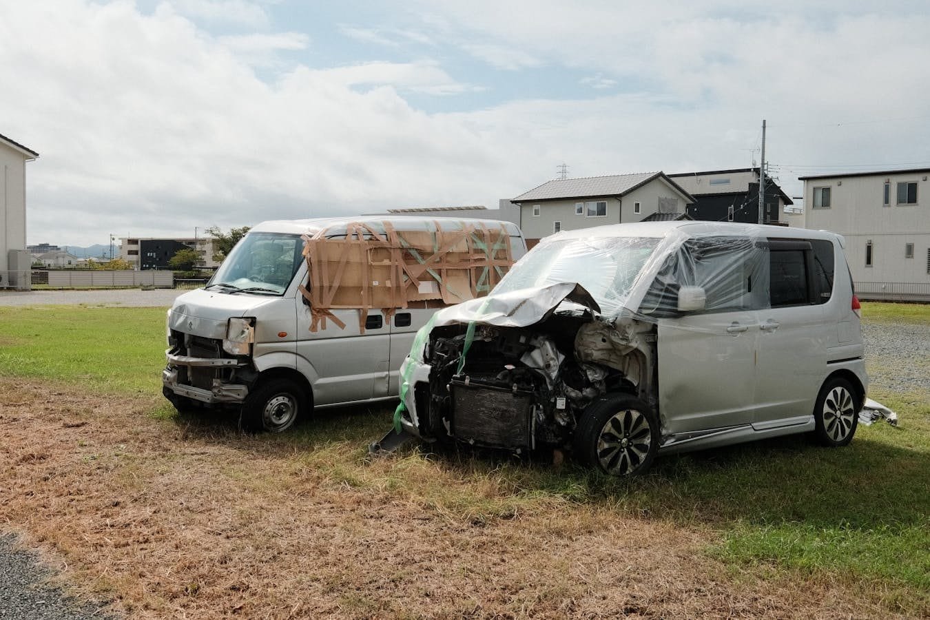 Two wrecked vans parked on a grassy area in Toyokawa, Japan.