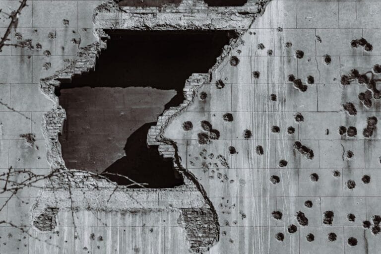 A dynamic black and white photo of a damaged concrete wall, featuring a large hole and multiple bullet impact marks, sym