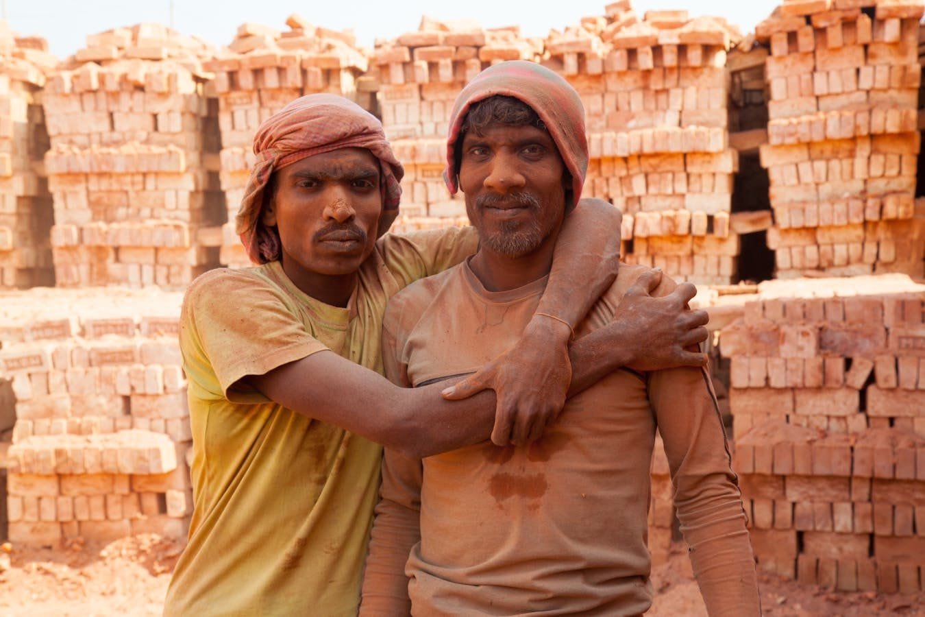 Two brick workers posing outdoors in a brickfield in Gabtoli, Dhaka, Bangladesh, showcasing camaraderie and hard work.