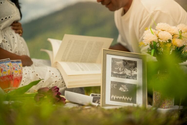 Couple reading with ultrasound photo, celebrating pregnancy amid nature in a serene outdoor setting.