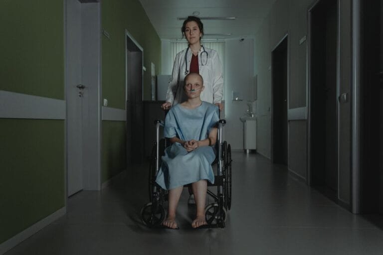 Doctor assisting female patient in wheelchair in dimly lit hospital hallway.