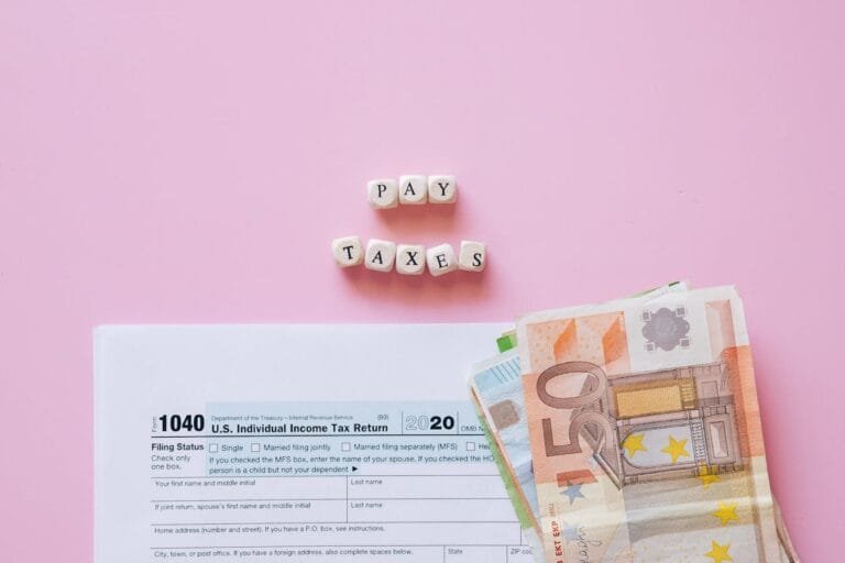 Top view of tax form, euro banknotes, and Pay Taxes letter blocks on pink background.