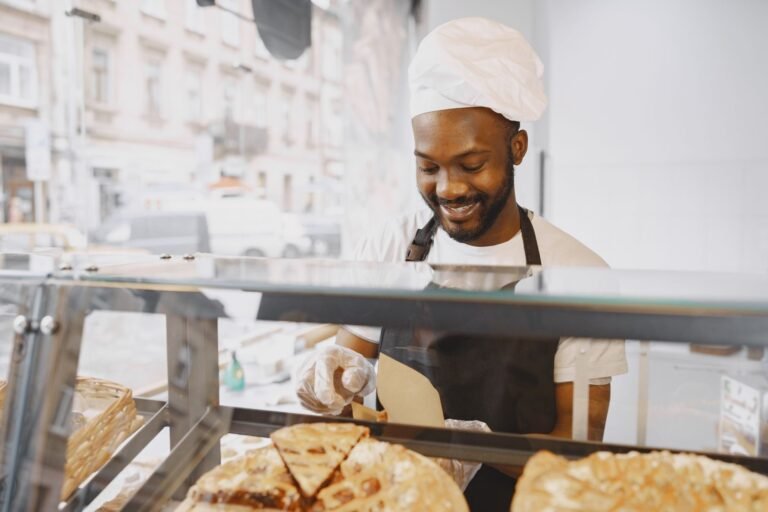 A cheerful baker in an apron serves pastries in a bright bakery display.