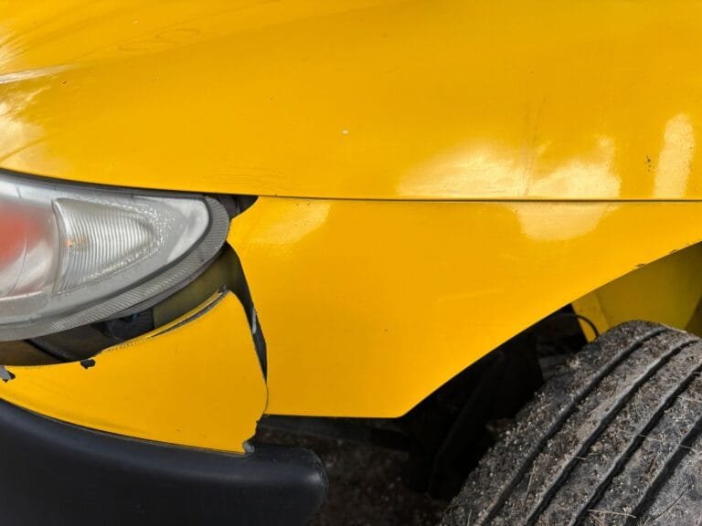 Acidente de transito: como funciona a reparação dos prejuízos 3 Close-up image of a yellow car's damaged front bumper and headlight for insurance or accid