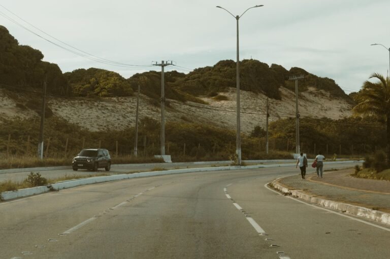 A peaceful road view in Natal, Brazil, featuring hilly terrain, a car, and pedestrians und