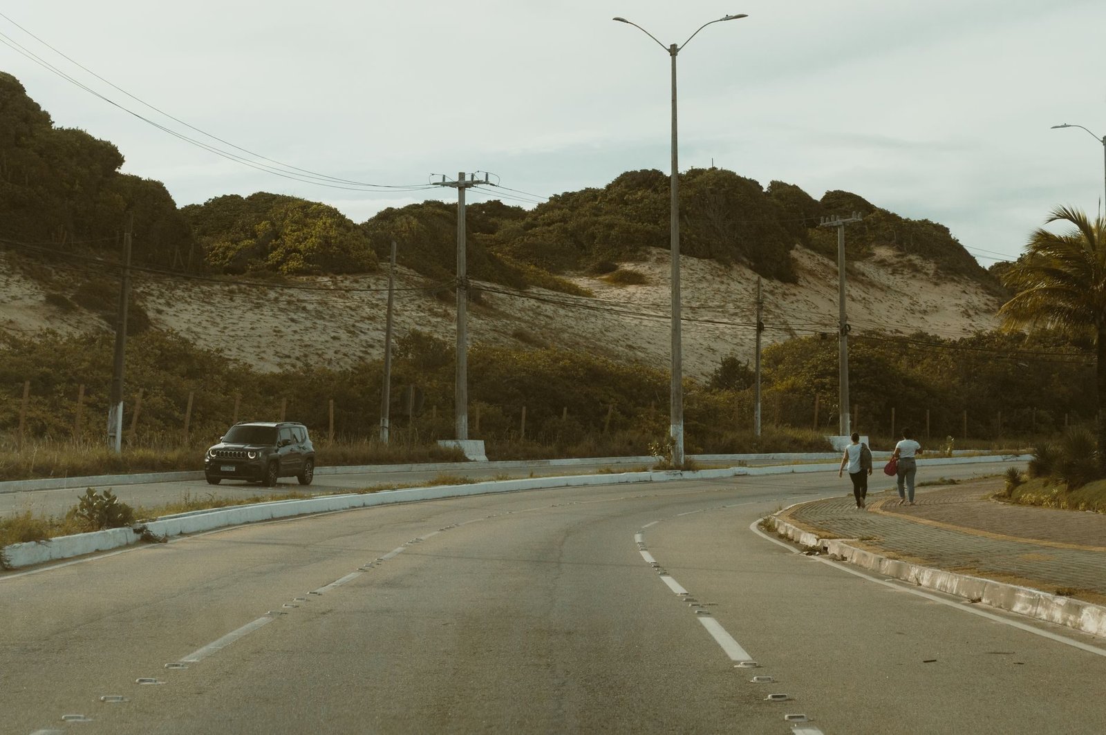 Acidente de transito: como funciona a reparacao dos prejuizos 1 A peaceful road view in Natal, Brazil, featuring hilly terrain, a car, and pedestrians und