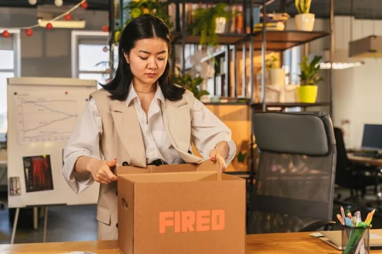 Acordo de não competição: até onde a empresa pode restringir o ex-empregado 5 An Asian woman packs a box labeled FIRED, symbolizing job loss in an office setting.