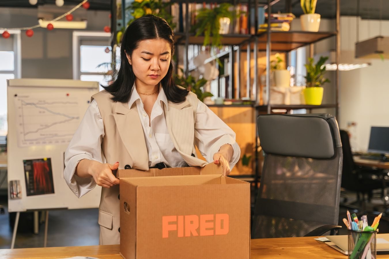 Acordo de nao competicao: ate onde a empresa pode restringir o ex-empregado 1 An Asian woman packs a box labeled FIRED, symbolizing job loss in an office setting.