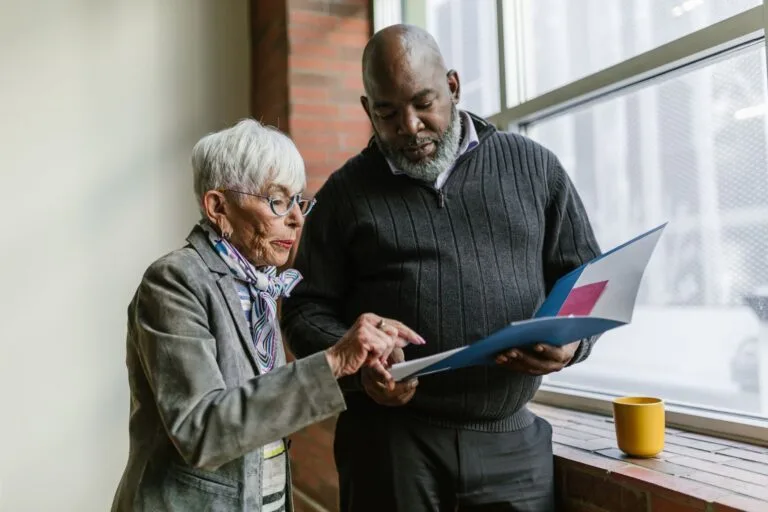 Senior colleagues working together, reviewing documents near an office window.