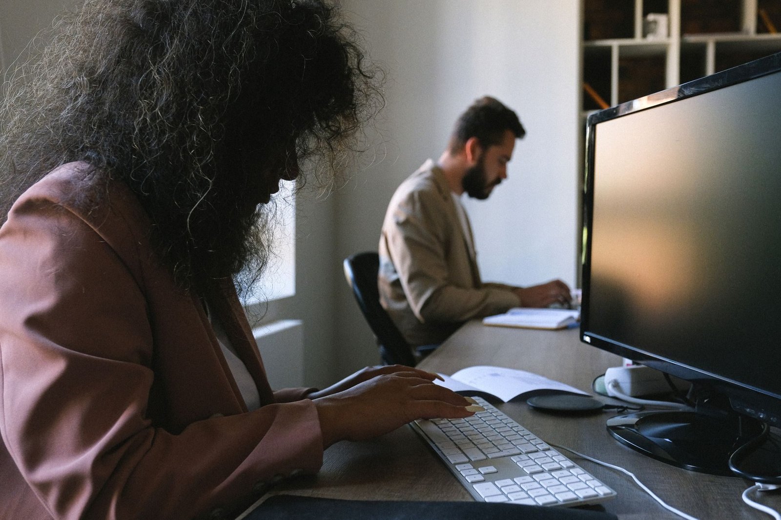 Side view of concentrated woman and man in formal wear typing on computers while sitting a