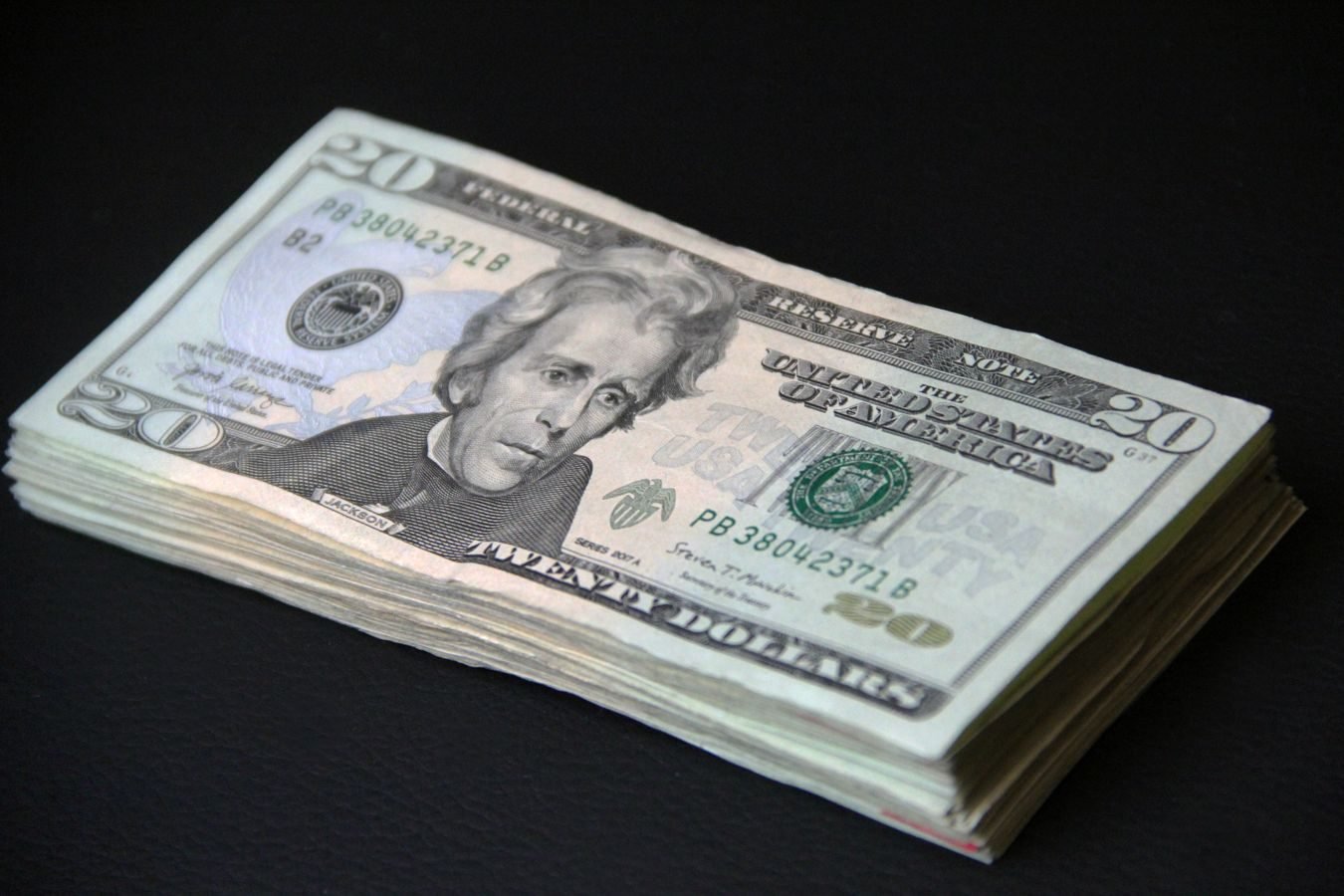 AGU obtém bloqueio de mais R$ 500 milhões e total de bens indisponibilizados em fraudes do INSS chega a R$ 4,5 bilhões 1 A close-up of a stack of American 20 dollar bills against a black background, symbolizing wealth.