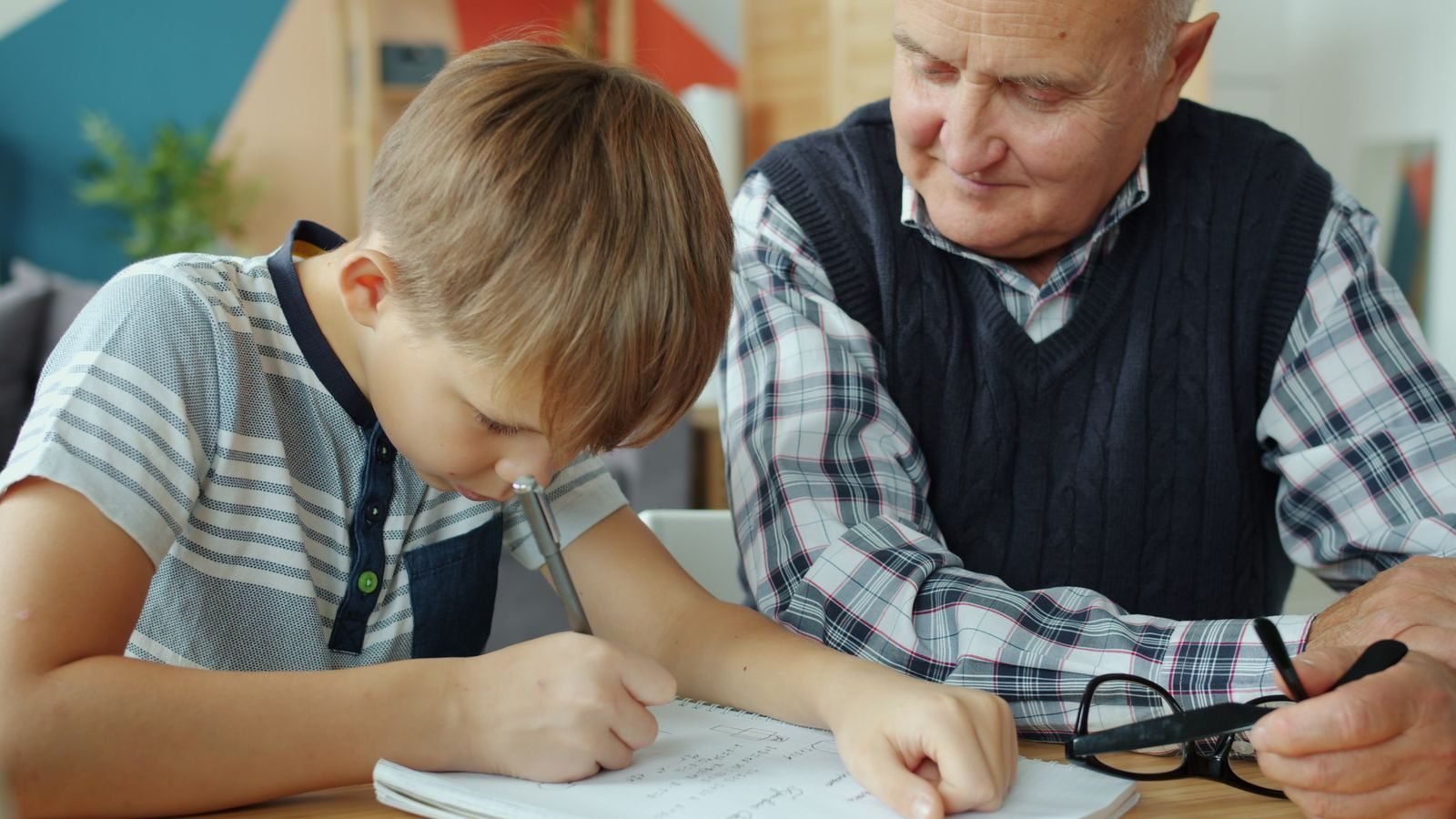 Elderly man assisting young boy with homework, fostering learning and bonding.