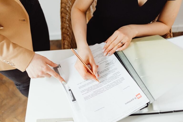 Alteracao e aditamento do contrato administrativo: limites das mudancas 3 Two women signing important documents at an office desk, showcasing teamwork.