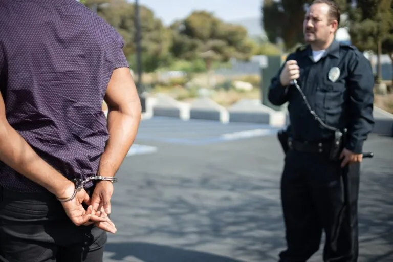 Ameaça e perseguição: limites entre desentendimento e crime 4 Police officer engaging with a handcuffed individual in an outdoor setting.