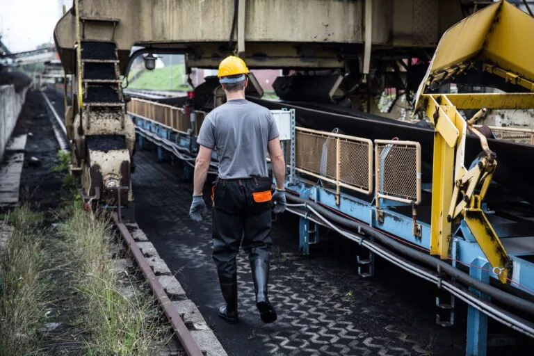 A worker in safety gear examines industrial machinery in an outdoor setting, showcasing industry work.