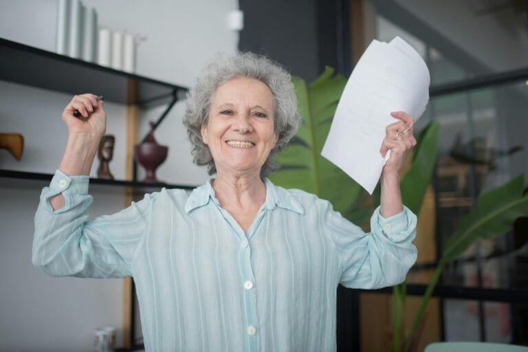 Aposentadoria por Tempo de Contribuicao: O Que Mudou Apos a Reforma 2 Joyful elderly woman holding documents inside an office setting, celebrating success.