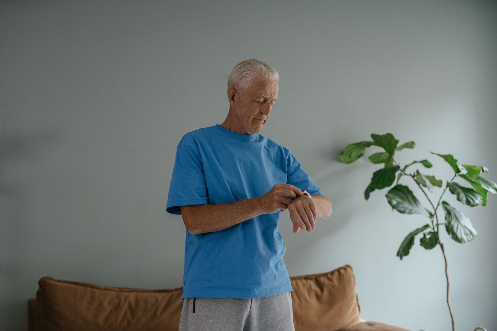 Aposentadoria programada: o que é e como funciona 1 Elderly man in a blue shirt checking his wristwatch indoors by a plant.