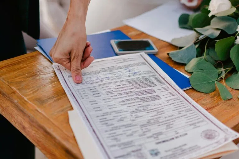 Atestmed 2026: Perícia Médica à Distância no INSS Expandida 6 Person pointing at a marriage certificate on a wooden table.