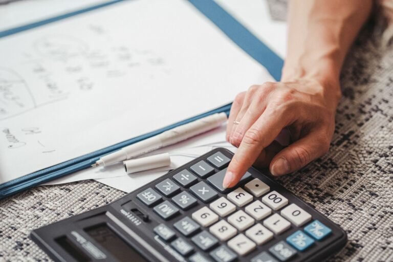 A hand using a calculator on top of documents, indicating financial calculation or analysi