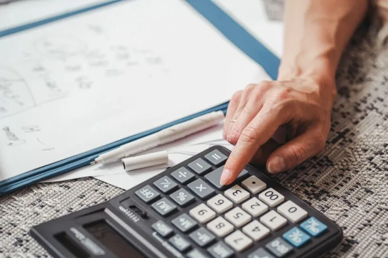 A hand using a calculator on top of documents, indicating financial calculation or analysi