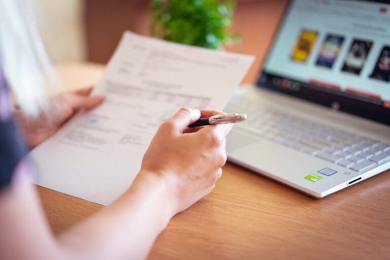 Bloqueio Arbitrário de Contas Digitais: Seus Direitos 2026 2 Close-up of a hand holding a pen and paper near a laptop, suggesting online shopping or document review.