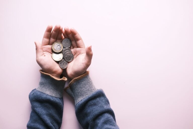 Close-up of hands in sweater holding various coins, indicating savings and finance on a wh