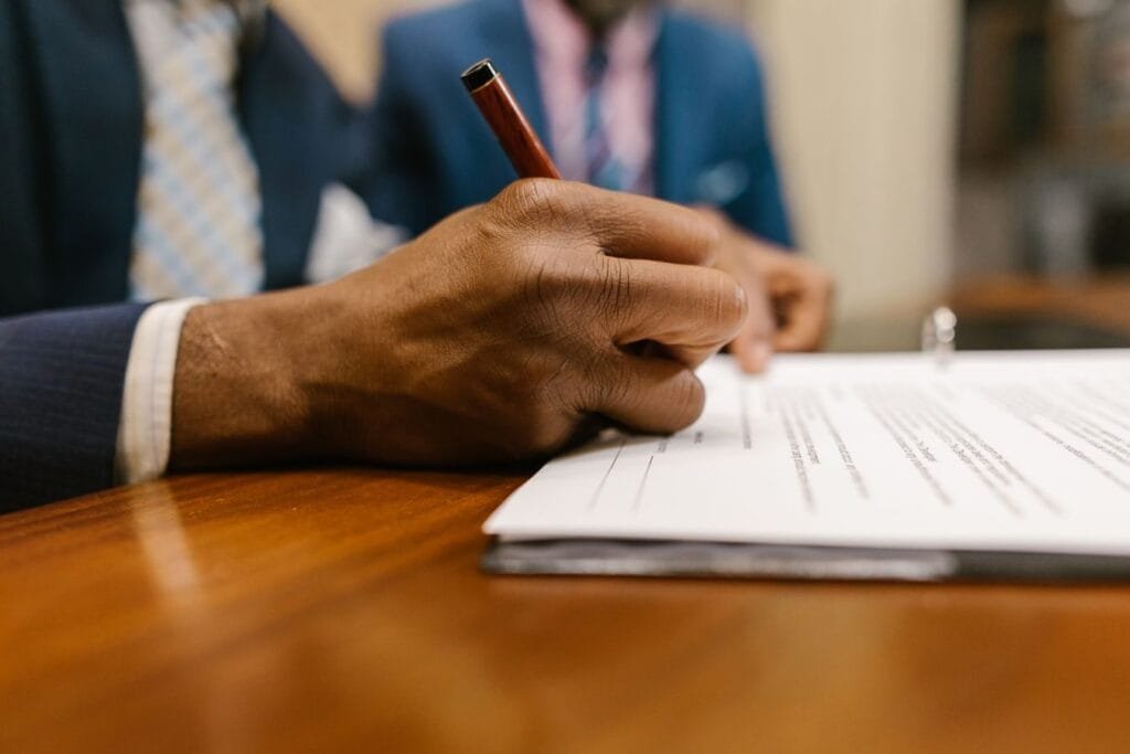 Tenho deficiência e pouca renda. Como funciona o BPC/LOAS para PCD? 1 Close-up of an adult signing a legal document with a pen in an office.