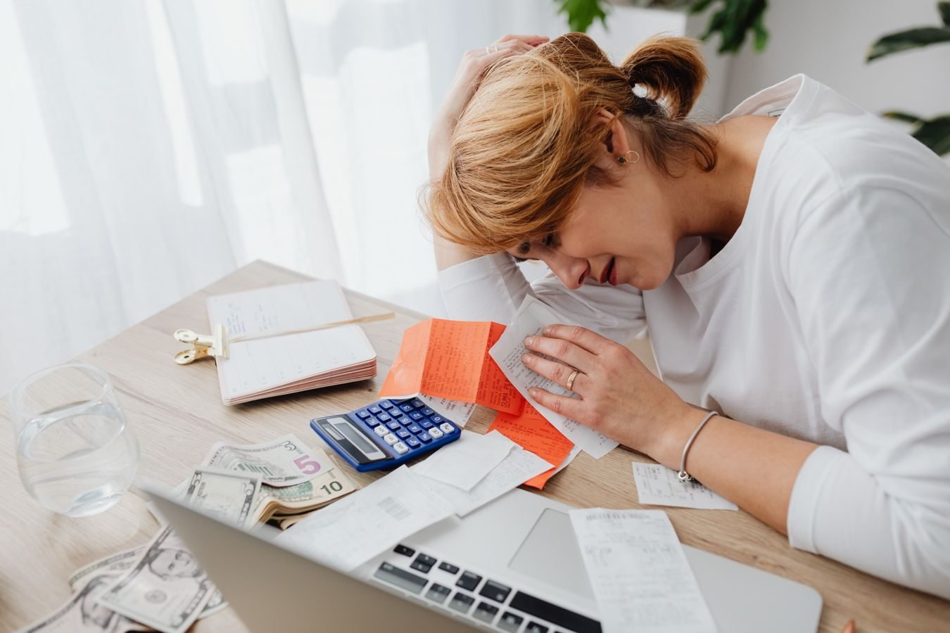 Cobranca abusiva de divida: limites do credor e direitos de quem deve 1 A woman overwhelmed with finances, surrounded by bills, calculator, and cash at home.