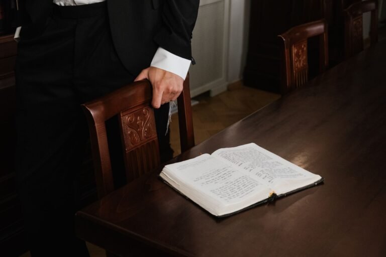 Elegant man in suit stands by a wooden table with an open book, indoor setting.