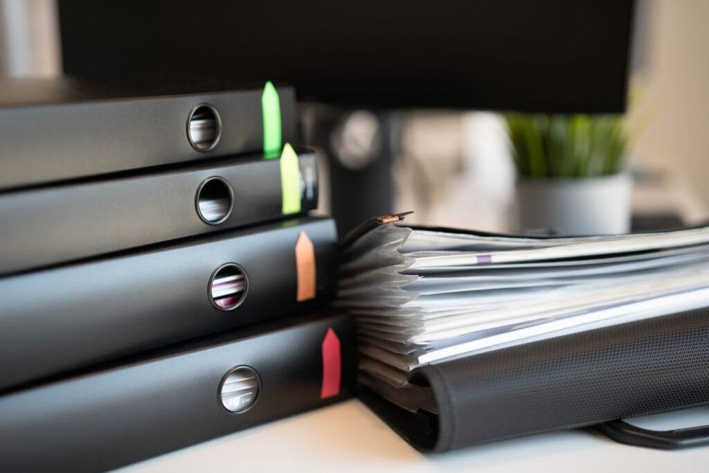 Como dou entrada na minha aposentadoria pelo INSS? 1 Stack of colorful ring binders and documents on a modern office desk setting.
