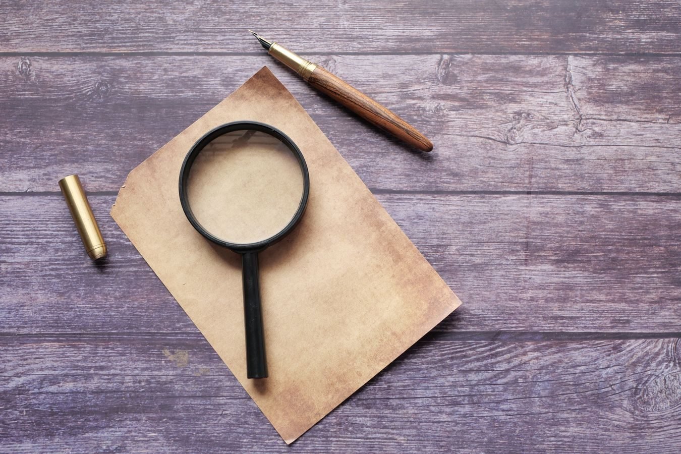Vintage quill pen with magnifying glass on rustic wooden surface. Perfect for retro-themed designs.