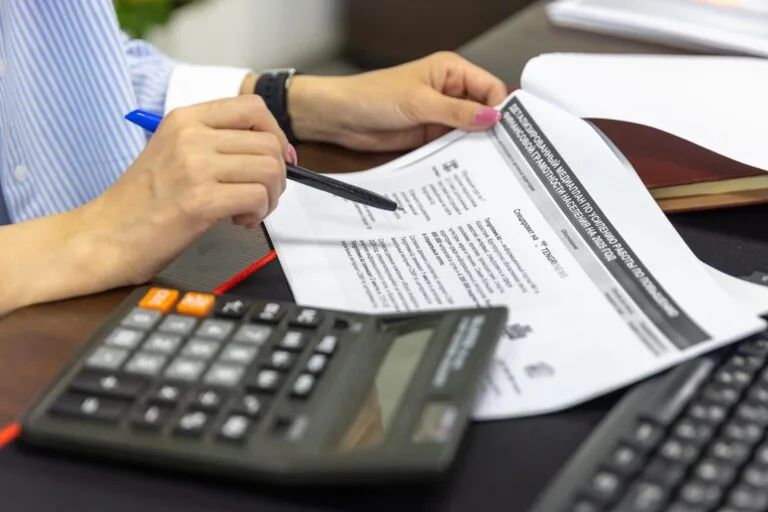 Compensação Tributária: Requisitos e Procedimento 5 Close-up of a person analyzing financial documents using a calculator and pen.