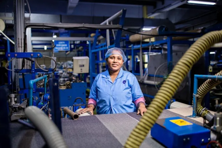 Female factory worker operating textile machinery in an industrial setting.