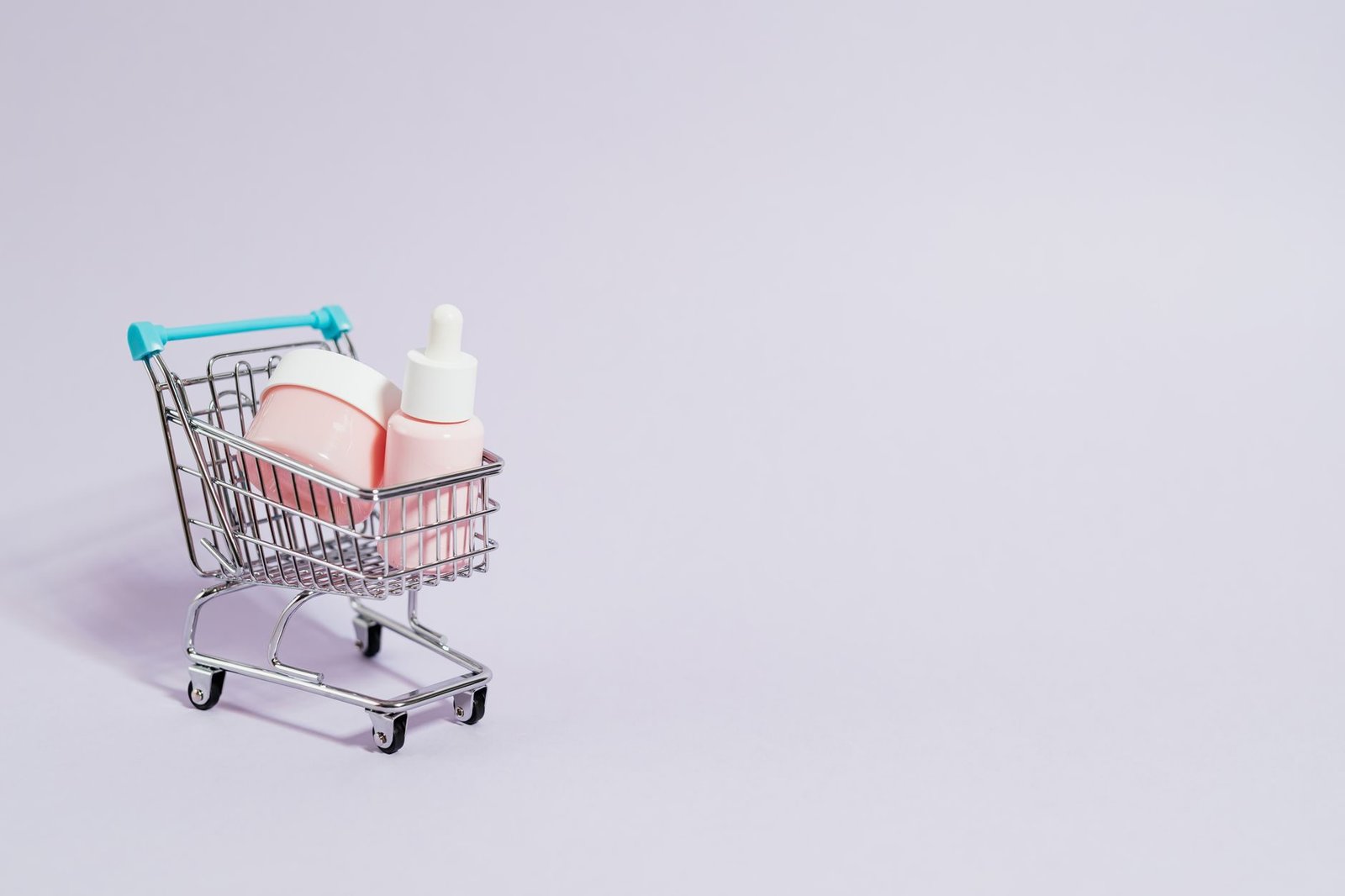 Comprei um produto que nao chegou: golpes em lojas virtuais e seus direitos 1 Small shopping cart holding pink skincare products on a pastel background.