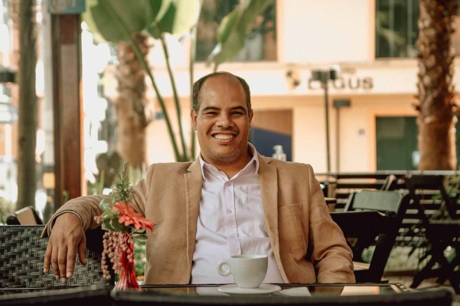 Conciliação e mediação para empresas: reduzindo litígios e preservando relações 1 Balding man in a suit jacket smiling while enjoying a coffee in an outdoor café setting.
