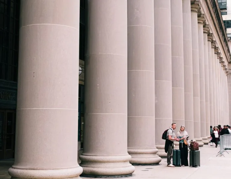 Two travelers stand beside large columns in Chicago, capturing the essence of urban explor