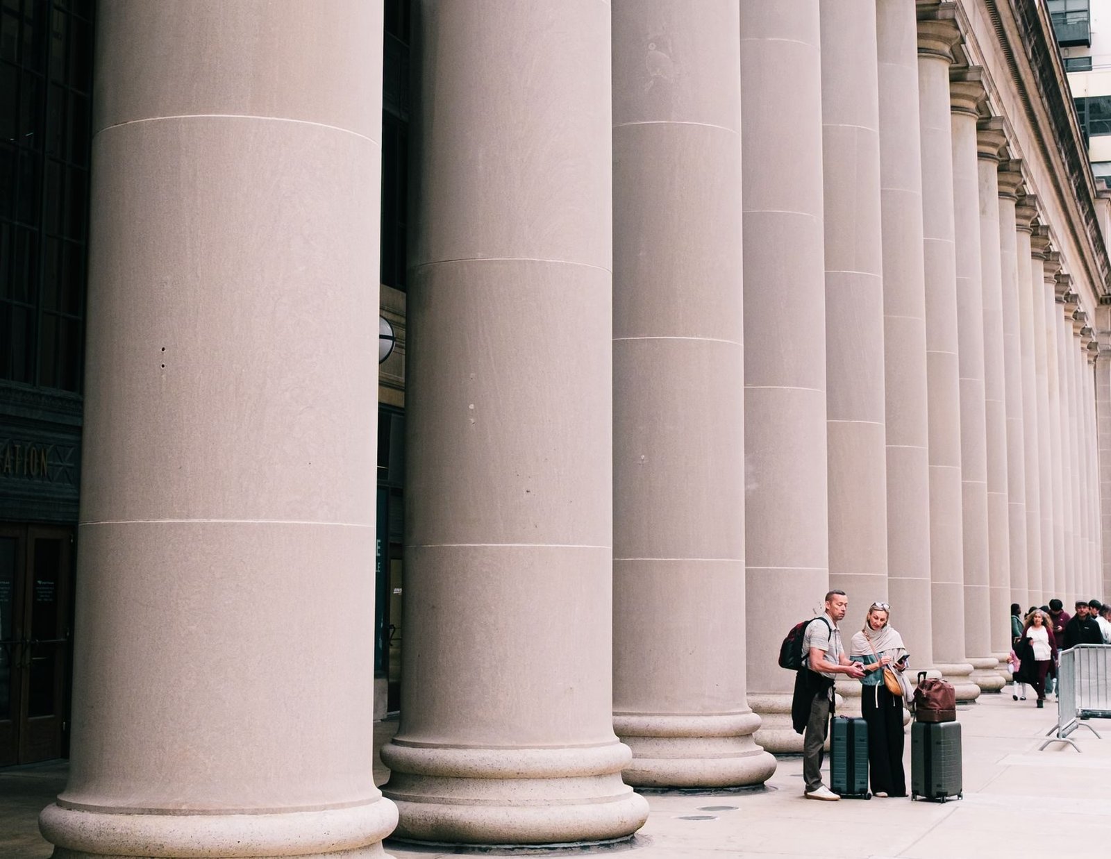 Two travelers stand beside large columns in Chicago, capturing the essence of urban explor