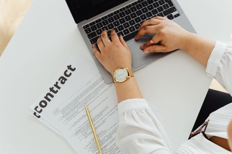 A woman using a laptop alongside a contract document on a desk, emphasizing business and l