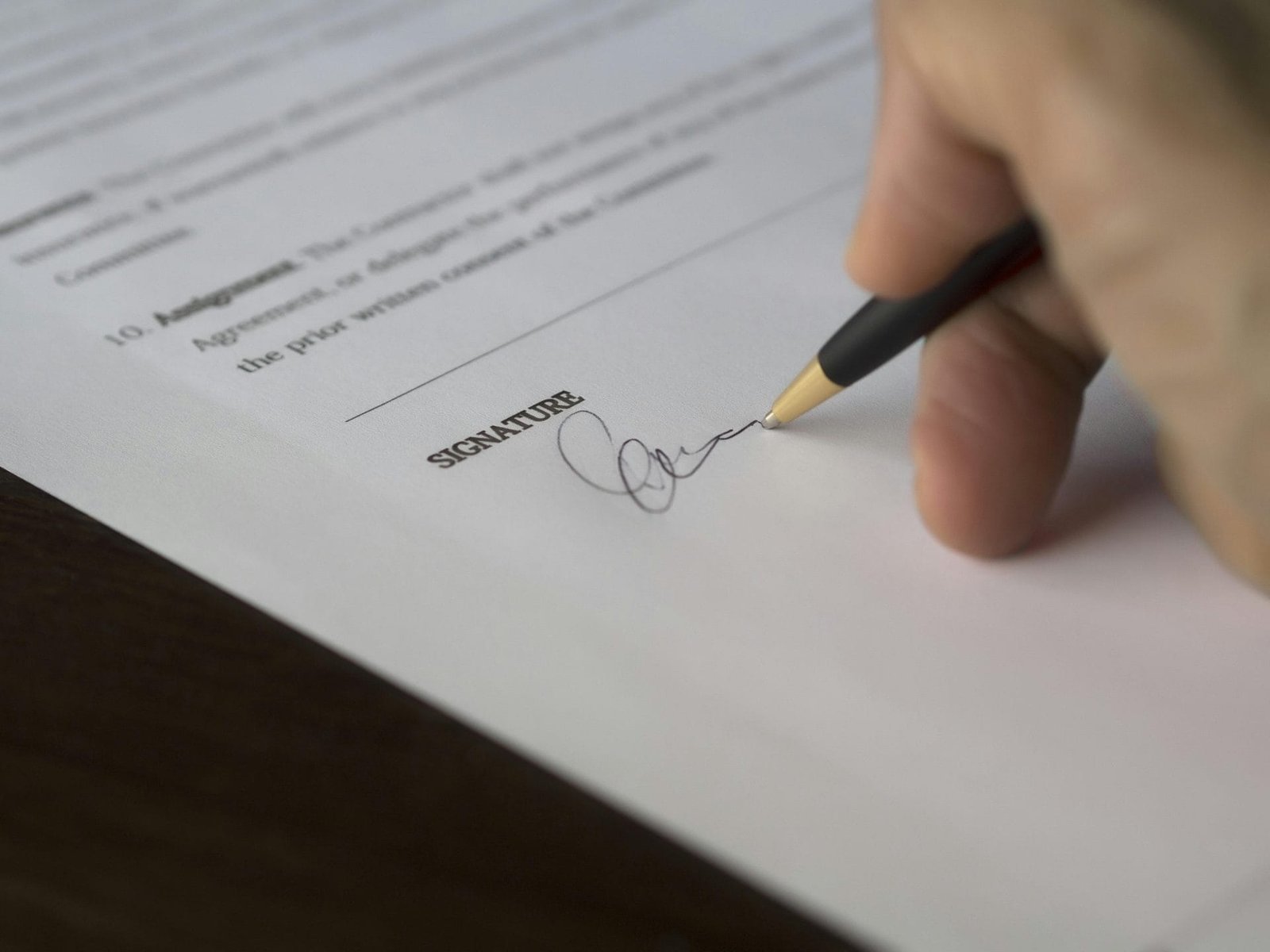 Contrato de Distribuição e Representação Comercial 1 A hand signs a formal contract with a pen on a wooden desk.