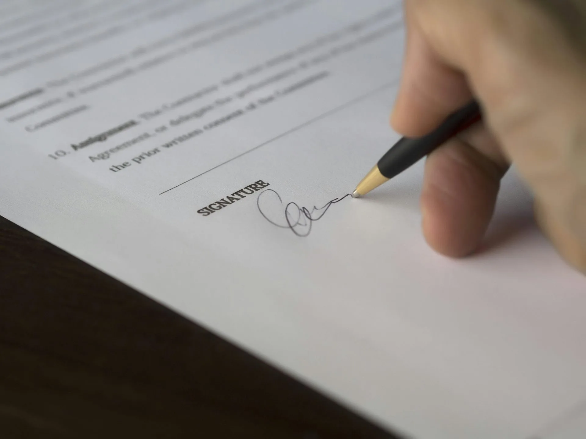 Contrato de Distribuição e Representação Comercial 1 A hand signs a formal contract with a pen on a wooden desk.