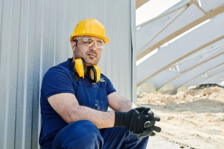 A male construction worker wearing safety gear sits at a construction site, showcasing sta