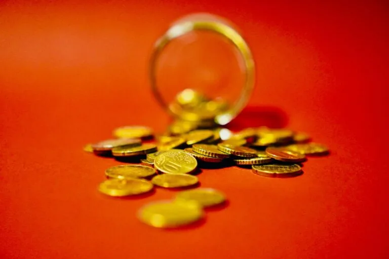 A collection of golden coins spilling from a glass jar on a vibrant red background symboli