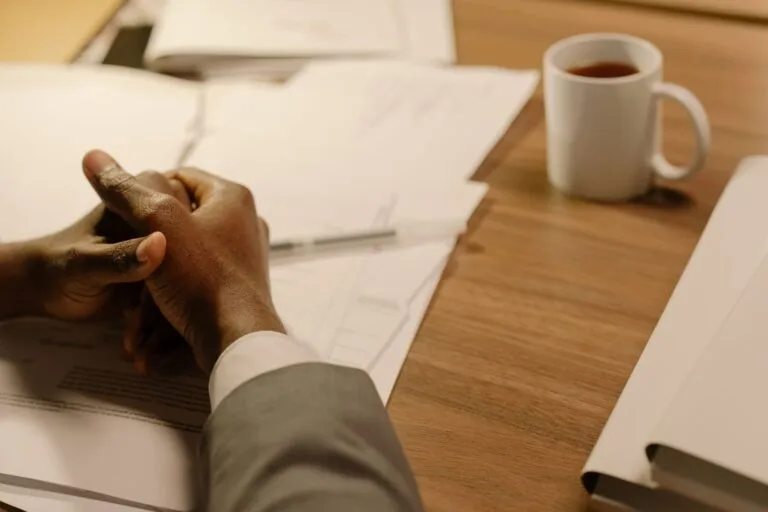 Close-up of a professional's hands at a desk with coffee and documents.