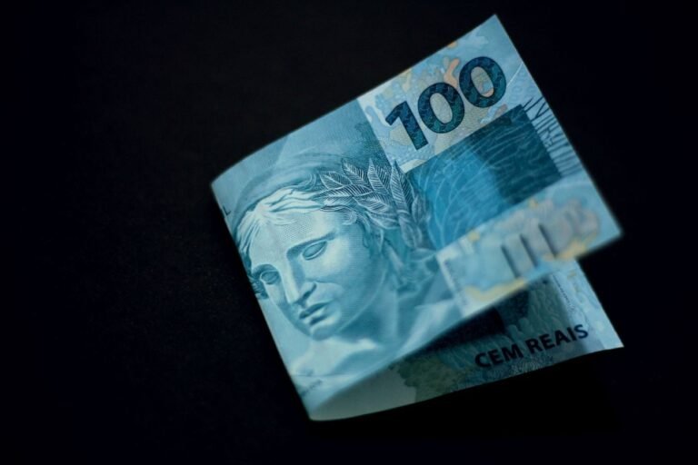 Decreto 12.797/2025 fixa salário mínimo em R$ 1.621,00 a partir de 1º de janeiro de 2026, reajuste de 6,79% 4 A Brazilian 100 real banknote displayed against a black backdrop, highlighting its design and color.