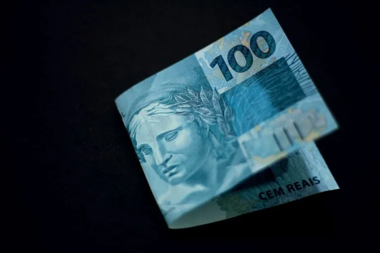 A Brazilian 100 real banknote displayed against a black backdrop, highlighting its design and color.