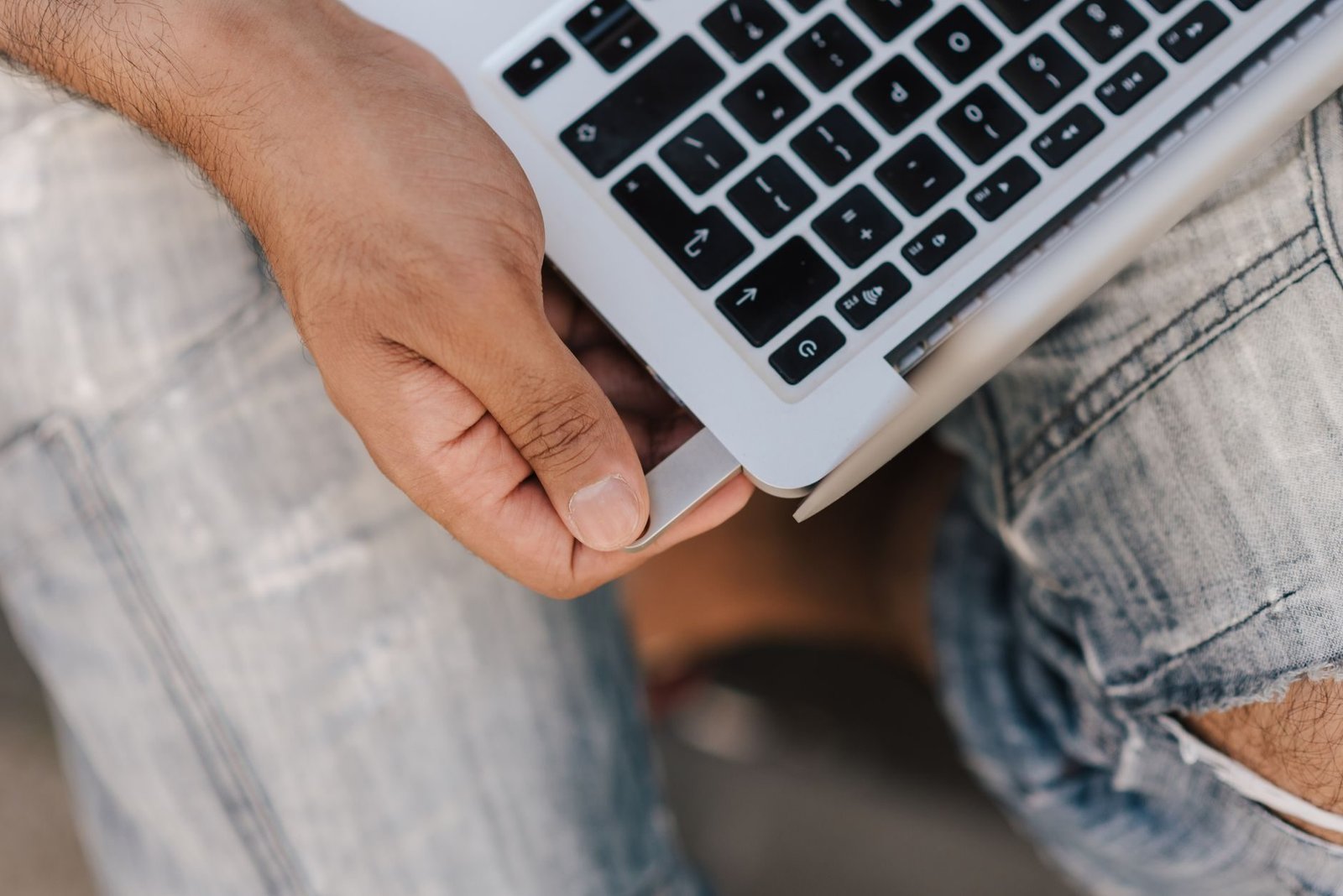 Top view crop faceless male in ripped jeans using netbook on laps and inserting memory car