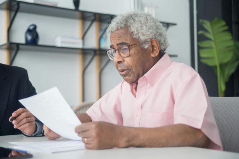 Demissão após Aposentadoria 2026: O que Diz a Lei e o TST 3 Elderly man with glasses reading a document in a home office setting, reflecting focus and concentration.